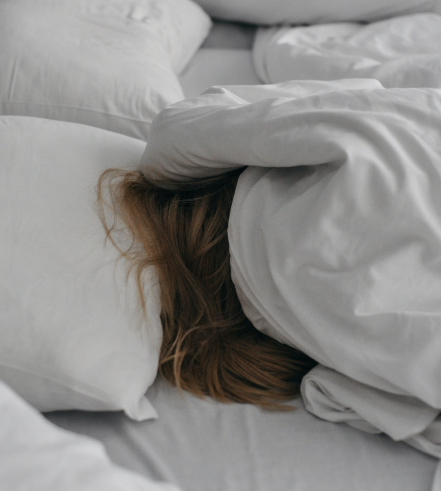 Woman lying in bed with covers pulled over her head.