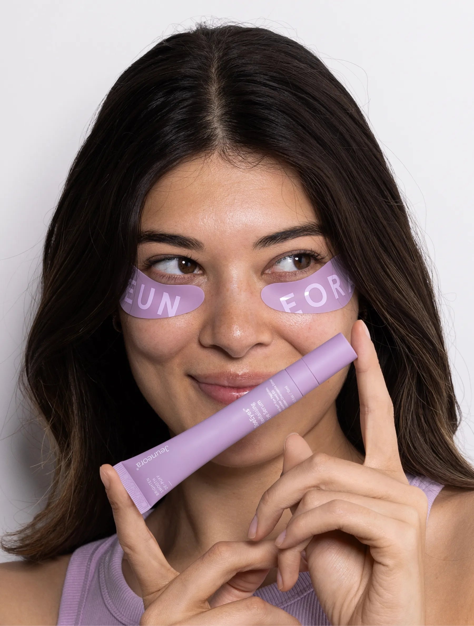 model posing with DoeEyes eye serum and reusable eye masks on purple background