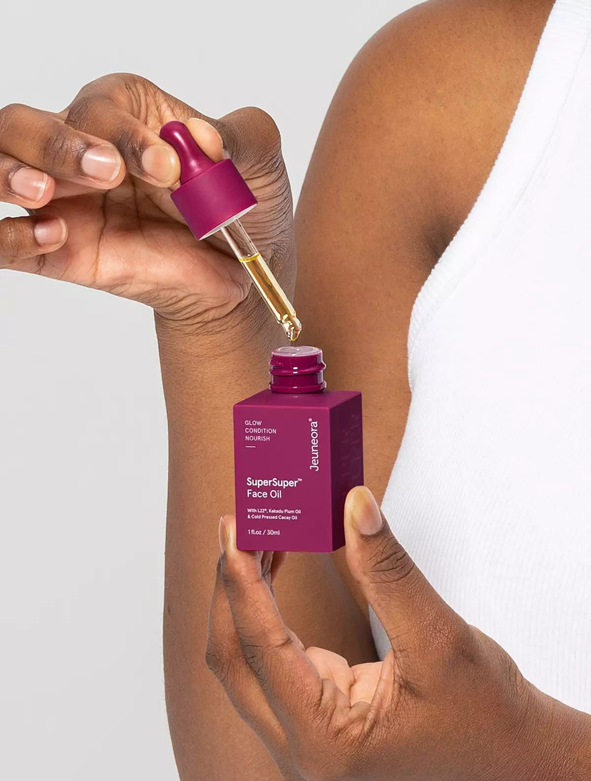 Jeuneora SuperSuper Face Oil dropper applying a drop of oil to the arm of a person in a white tank top