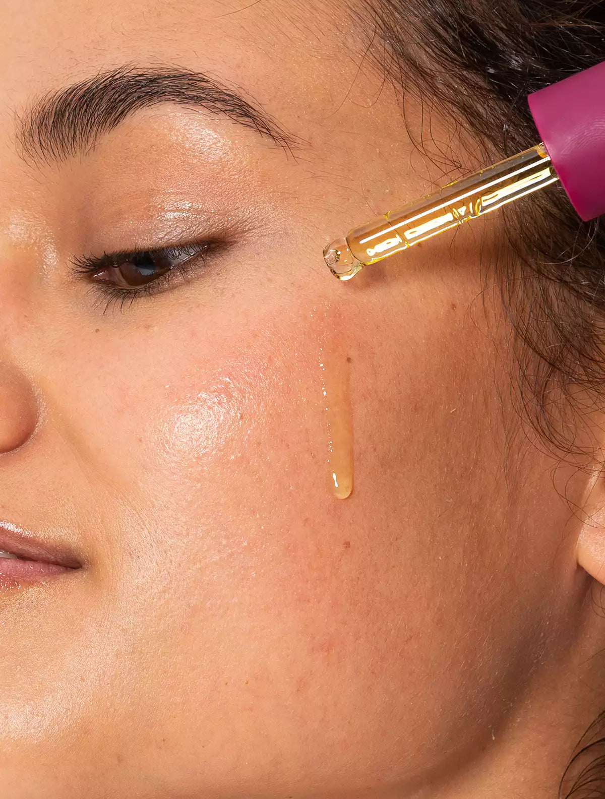 Close up of a drop of Jeuneora SuperSuper Face Oil being applied to a model's cheek with the dropper